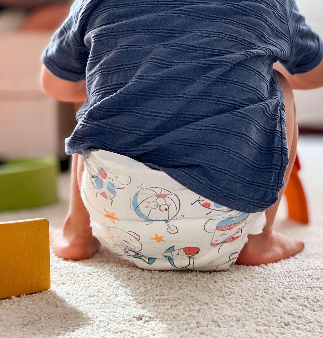 A toddler in Mum & You eco-friendly nappy pants sits on the floor surrounded by colorful toys, happily engaged in playtime activities.