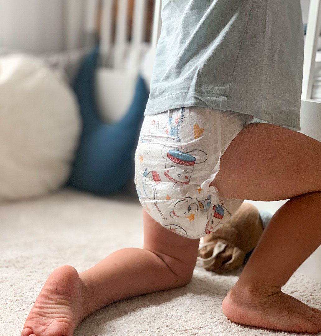 A toddler in Mum & You nappies stands on the floor, capturing a playful and innocent moment of early childhood.
